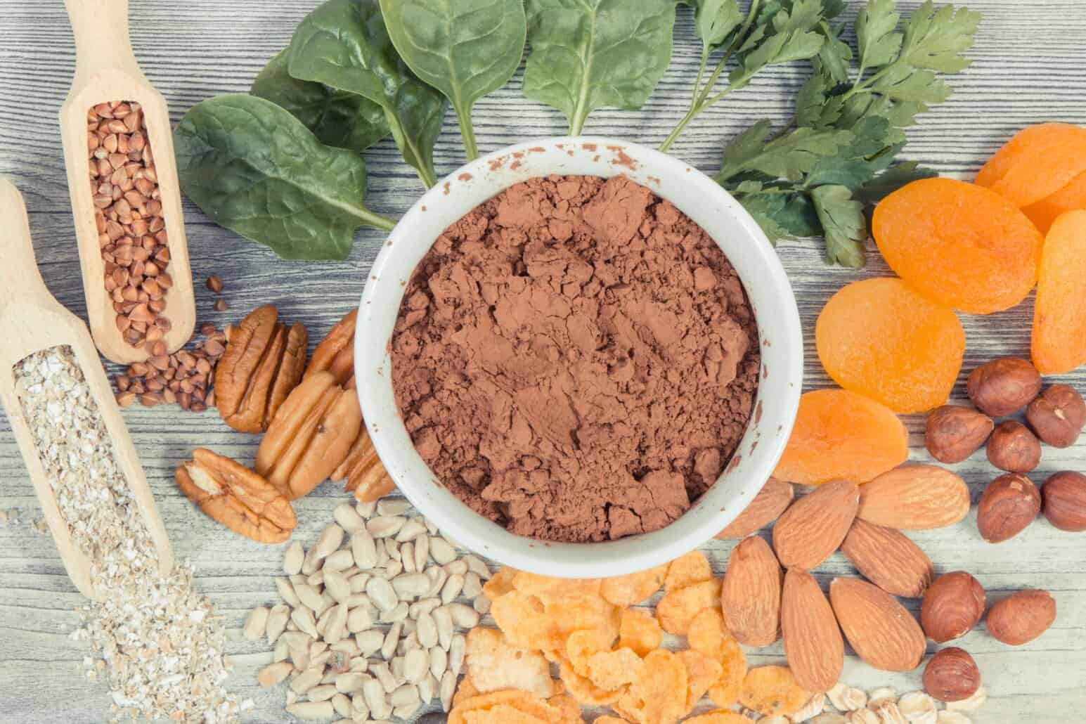 NutriFusion food ingredients with powder in a bowl, surrounded by nuts, seeds, dried fruit, and leafy greens.